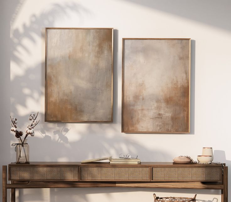 two paintings hang on the wall next to a console table with baskets and vases