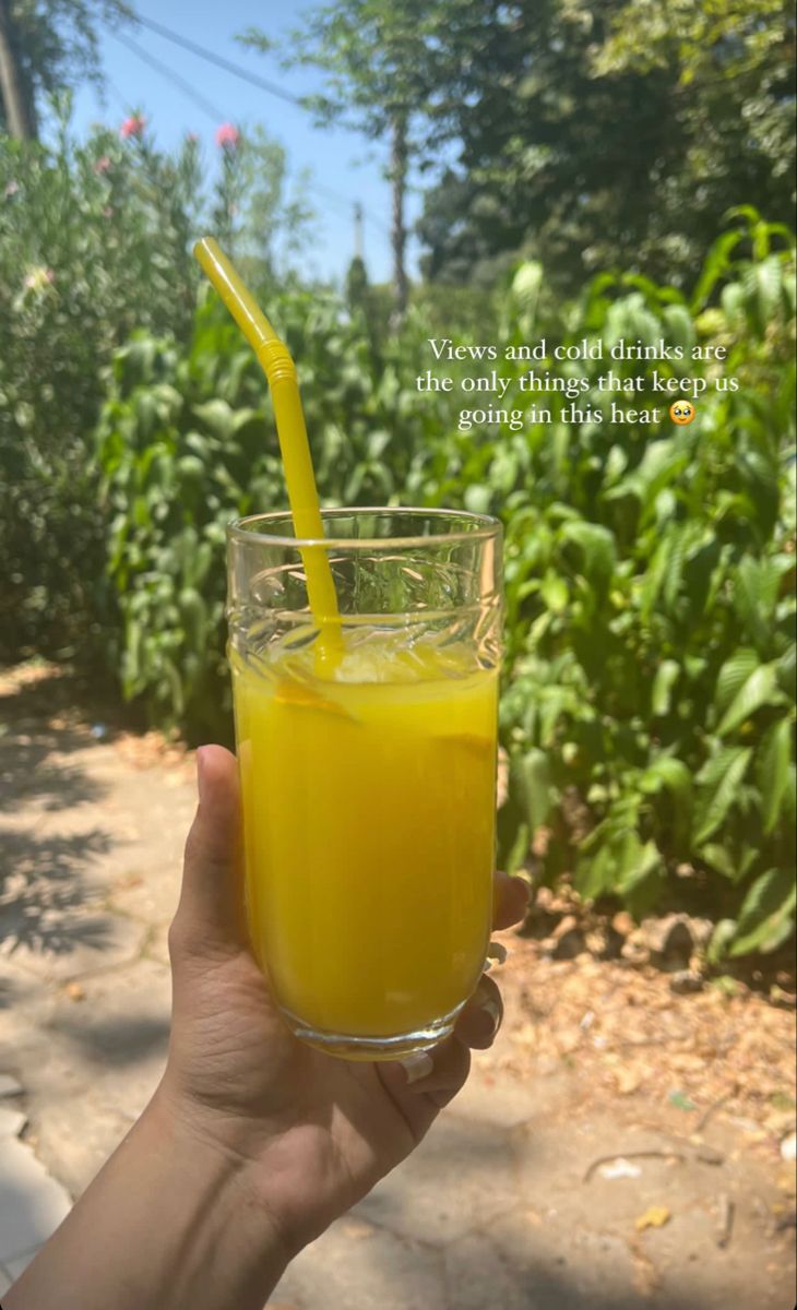 a person holding up a glass with orange juice in it and a straw sticking out of the top