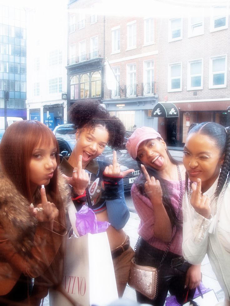 four girls are posing for the camera in front of a store window with their fingers up