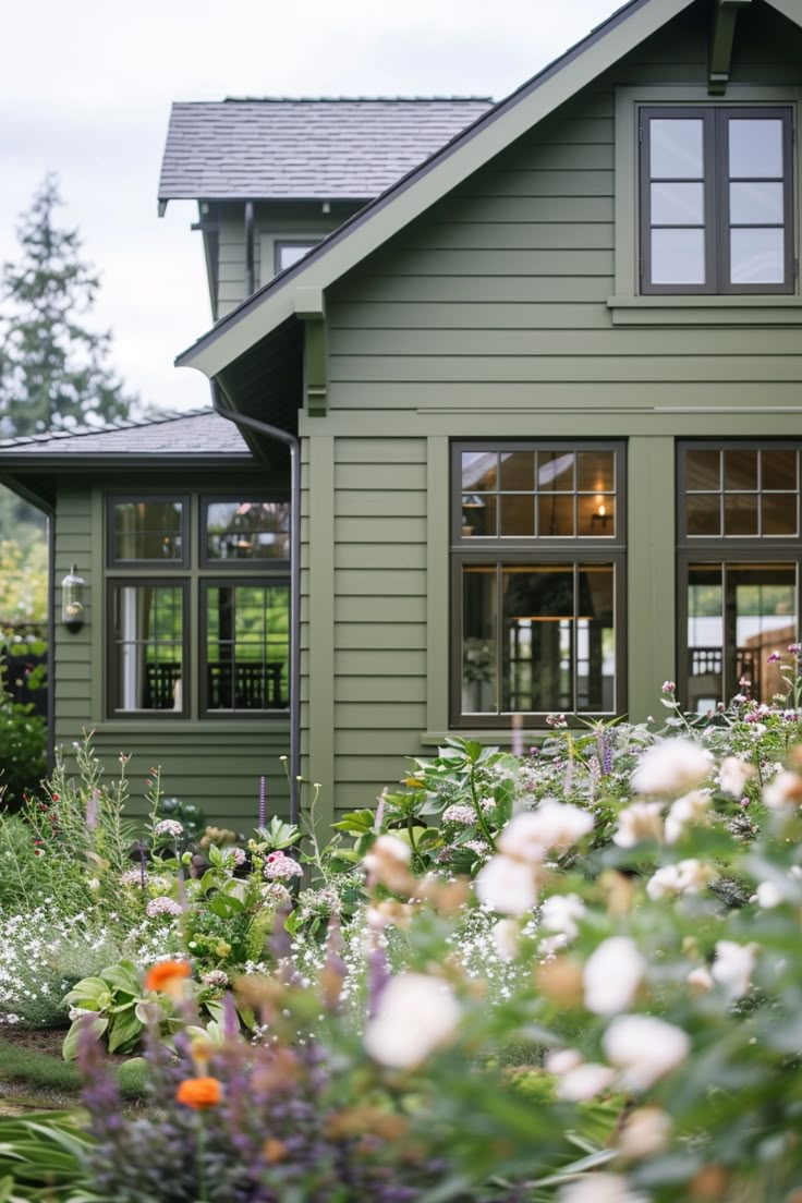 a green house with lots of flowers in the front yard and windows on each side