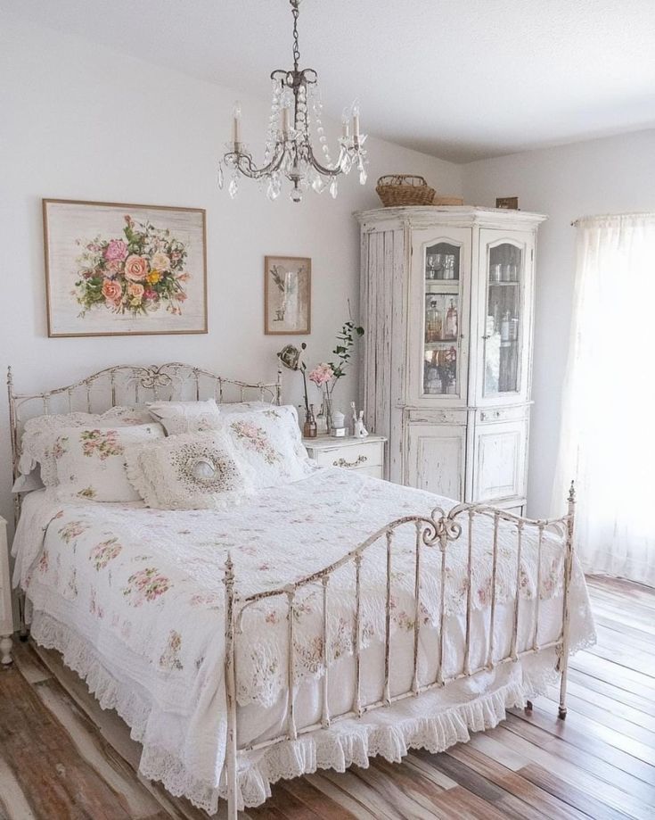 a white bed sitting inside of a bedroom next to a dresser and chandelier