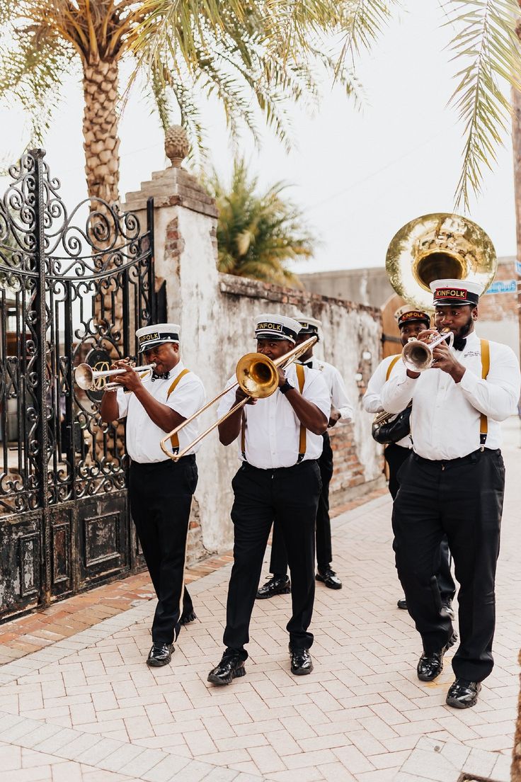 three men in white shirts and black pants are playing brass trombones on the sidewalk