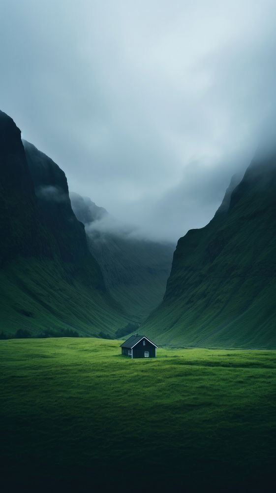 a green field with a house in the middle surrounded by mountains and foggy skies