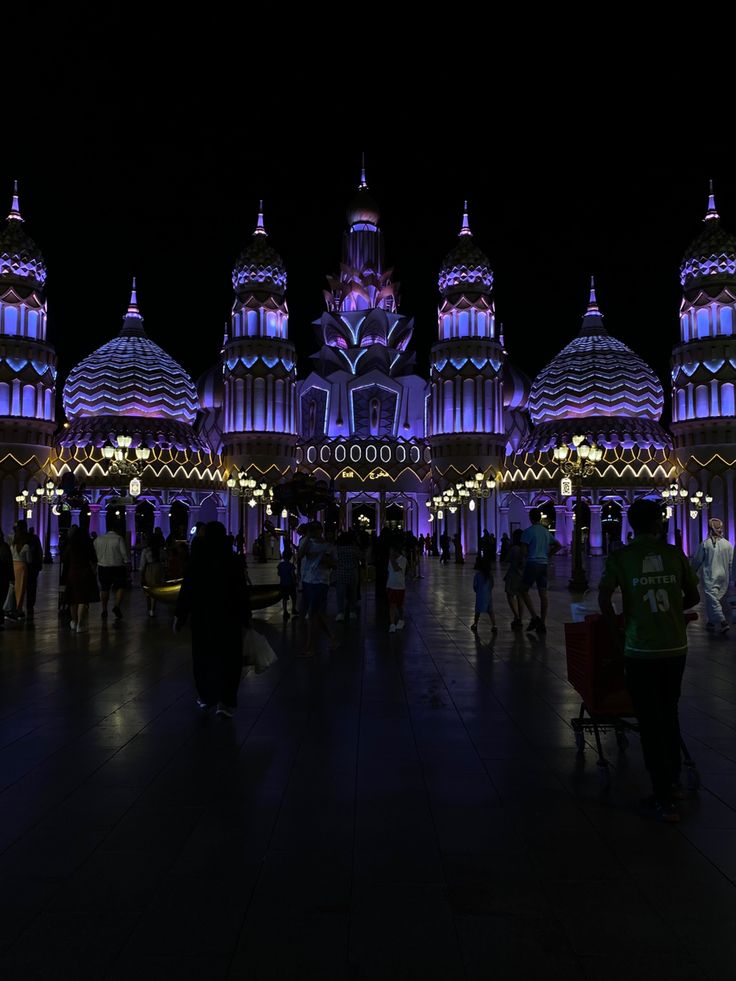 many people are walking around in front of some lit up buildings with lights on them