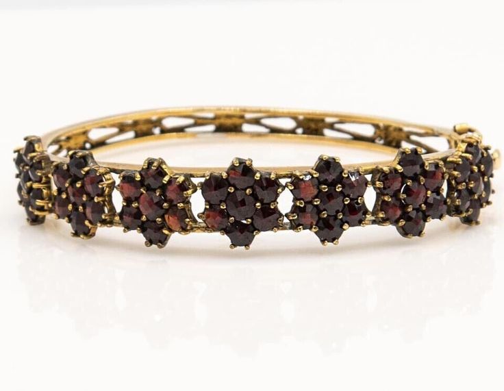 Antique bohemian garnet floral design 14k gold bangle bracelet Description  A stunning, rich, bountiful presentation of the garden's most precious blossoms, this Victorian bohemian garnet floral hinged bangle bracelet in solid 14k yellow gold is a beautiful treasure, sure to pamper you elegantly whenever you wear it. 7 Flowers of brilliant, fiery securely prong and bezel set garnets ( January Birthstone ) are made up of red round rose cut pyrope garnets! This luxurious bracelet has a hidden clasp safety latch and safety chain for security. This flower design bracelet is crafted in solid 14k gold with  round cut garnets prong set across the top half. The sides of the bangle are engraved with an ornate curling scroll reticulated design. The bracelet is hinged at the half and closes with a bo Luxurious Bracelet, 14k Gold Bangle Bracelet, Antique Bracelets, Design Bracelet, Garnet Jewelry, Safety Chain, January Birthstone, Gold Bangle Bracelet, Gold Bangle