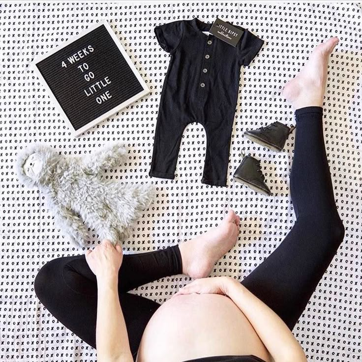 a pregnant woman laying on top of a bed next to shoes and a teddy bear