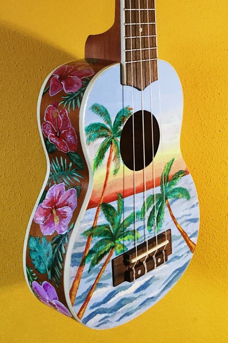 a painted ukulele hanging on a wall with flowers and palm trees in the background