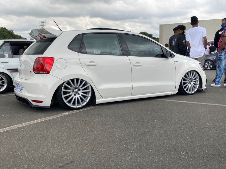 a white car parked in a parking lot next to other cars and people standing around