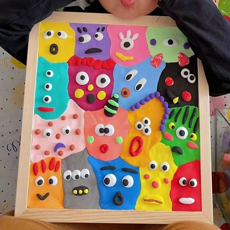 a young child holding up a colorful art piece with eyes and mouths on it's face