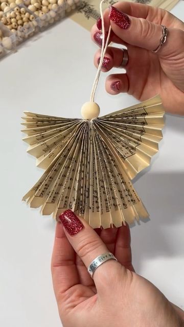 a hand holding a paper fan ornament in it's left hand and another hand with red nail polish on it