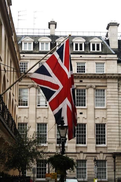 an union jack flag is hanging from a lamp post in front of a large building