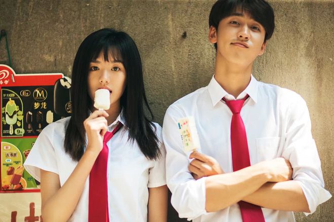 two young people standing next to each other with their arms crossed and eating ice cream