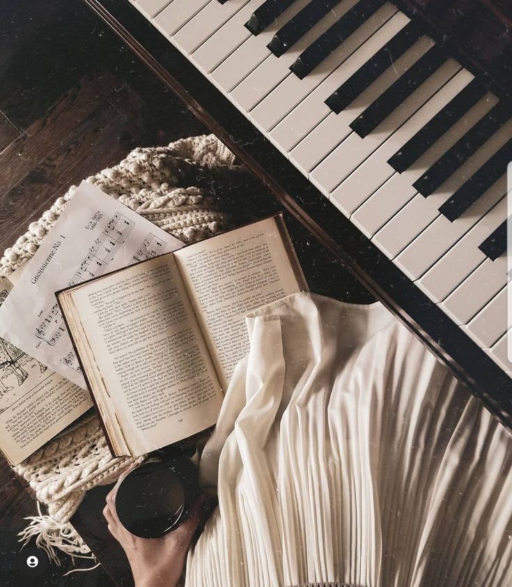 an open book sitting on top of a piano next to music sheets and a fan