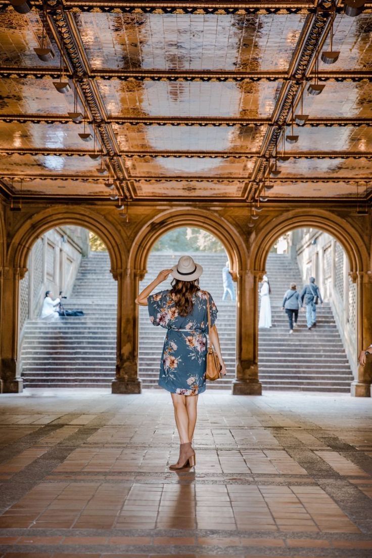 a woman in a blue dress and hat walking through an archway