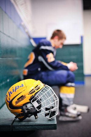 a young boy sitting on a bench next to a hockey goalie's helmet