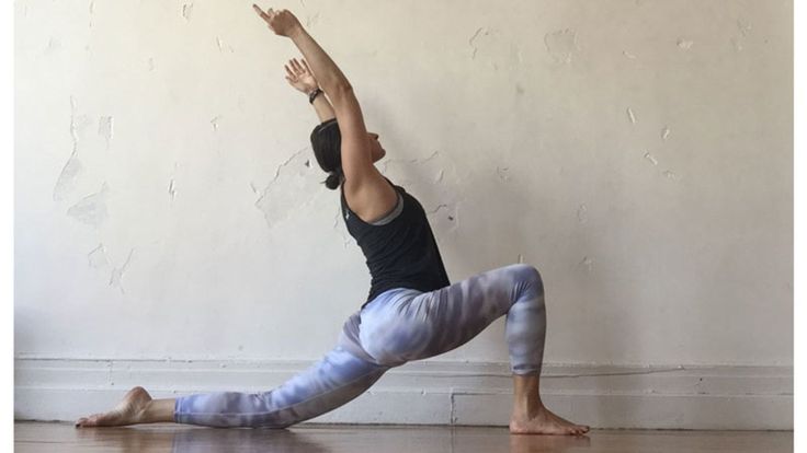 a woman is doing yoga in front of a wall with her hands up to the side