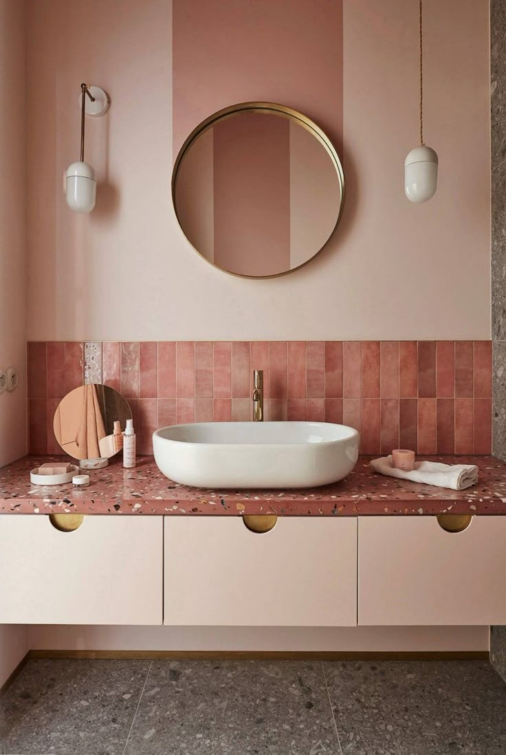 a bathroom with pink and gold walls, a round mirror above the sink and marble countertop