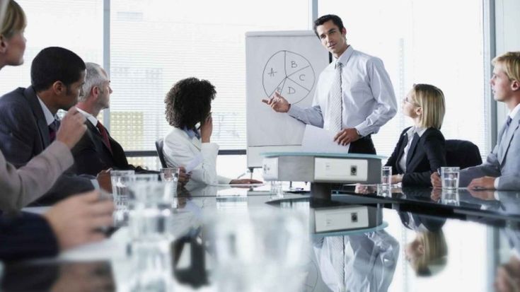 a group of people sitting around a conference table with a whiteboard in the middle