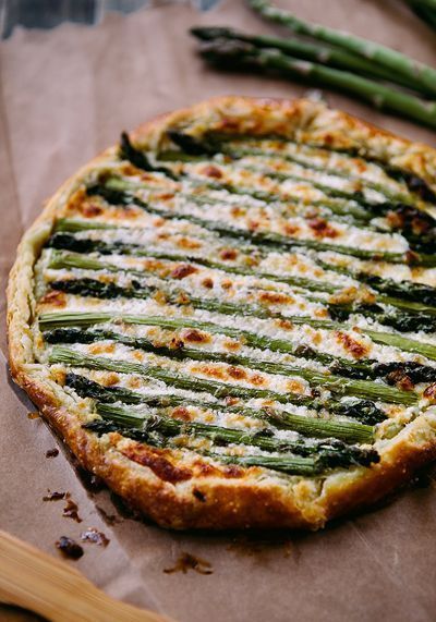 a pizza with asparagus and cheese is on a piece of wax paper next to some green beans