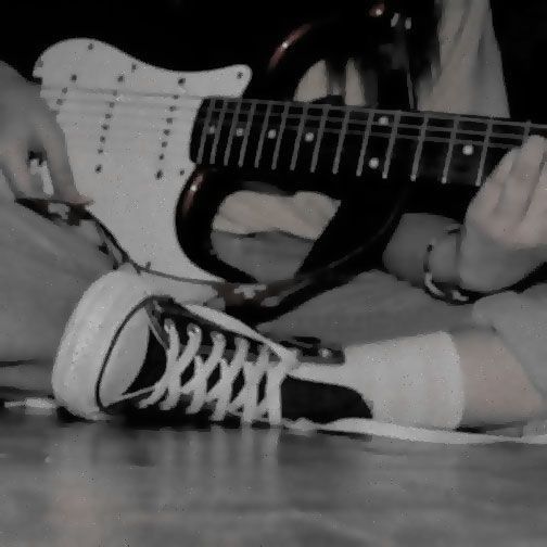 a person sitting on the floor with a guitar in their lap and one hand holding an electric guitar