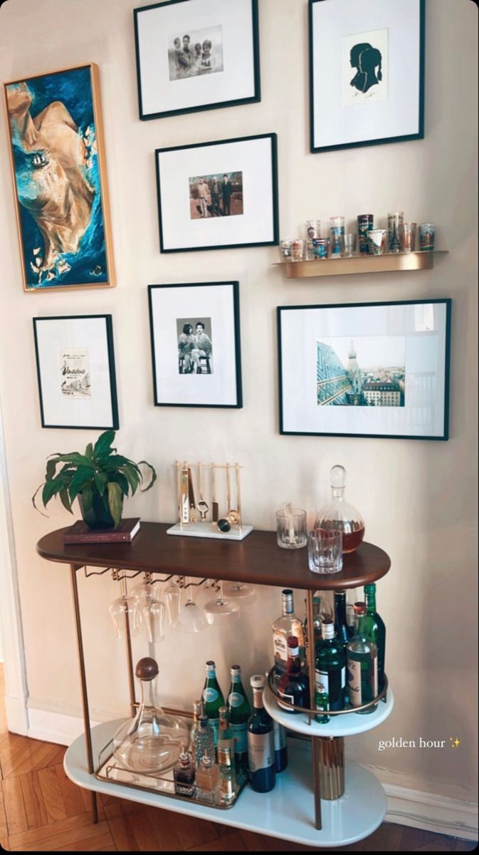 a bar cart with wine glasses and bottles on it in front of framed pictures hanging on the wall