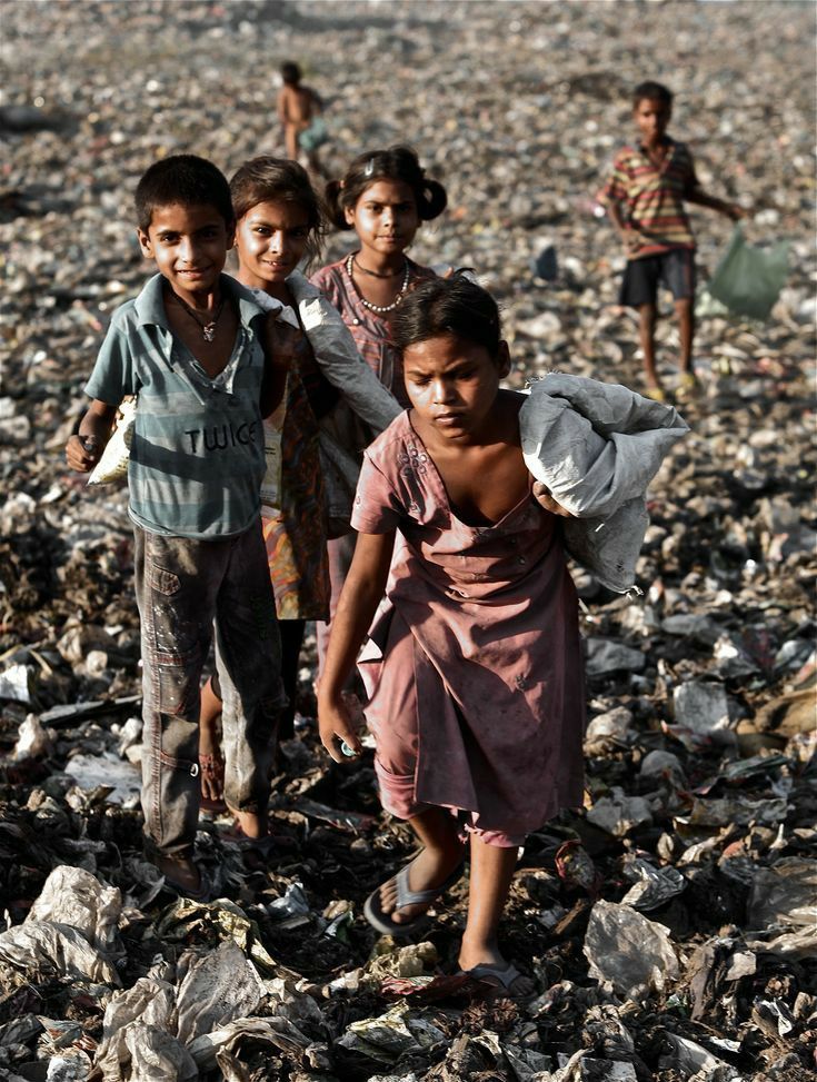 three children are walking through the rocks and debris in an open field, one is carrying a bag