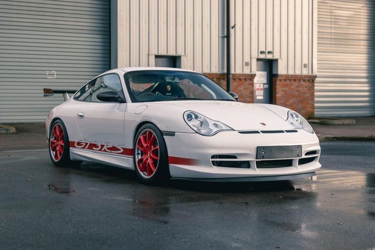 a white sports car with red rims parked in front of a warehouse building on a rainy day