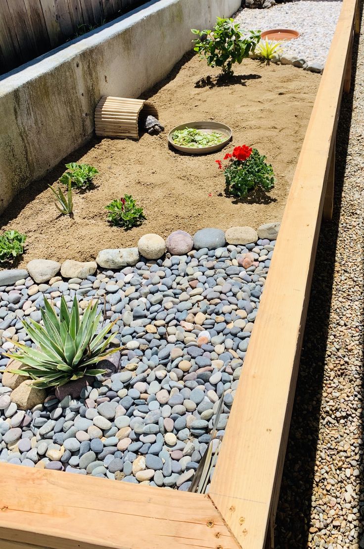 a wooden bench sitting next to a garden filled with rocks and plants on top of gravel