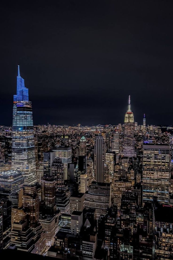 an aerial view of new york city at night with the empire building lit up in blue