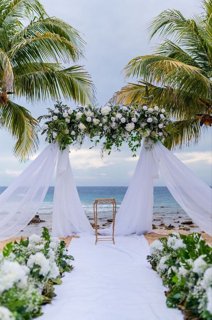 an outdoor wedding setup on the beach with white flowers and greenery in front of it