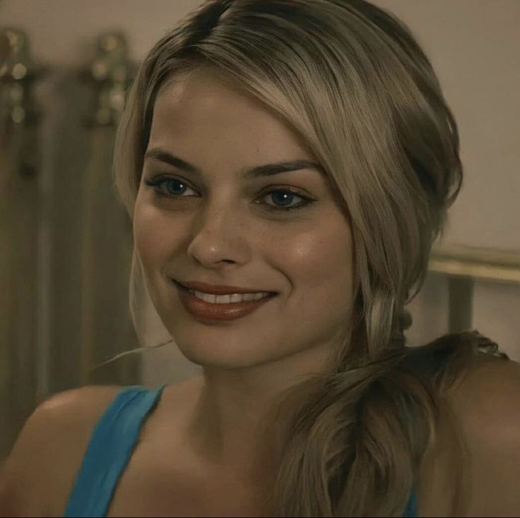 a woman with blonde hair and blue dress smiling at the camera while standing in front of a mirror