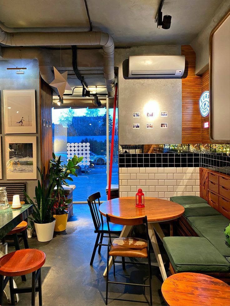 the inside of a restaurant with tables, chairs and plants on the counter top in front of an open door