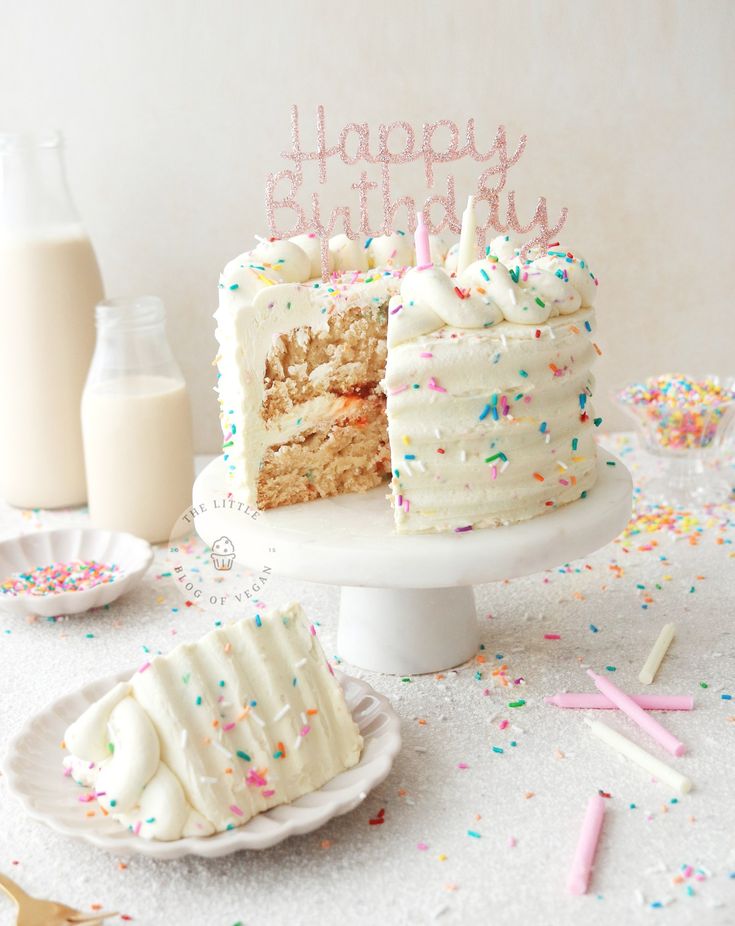 a birthday cake with white frosting and sprinkles sits on a table