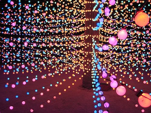 the lights are glowing brightly in the night sky and on the ground, there is a tree with many balls all over it