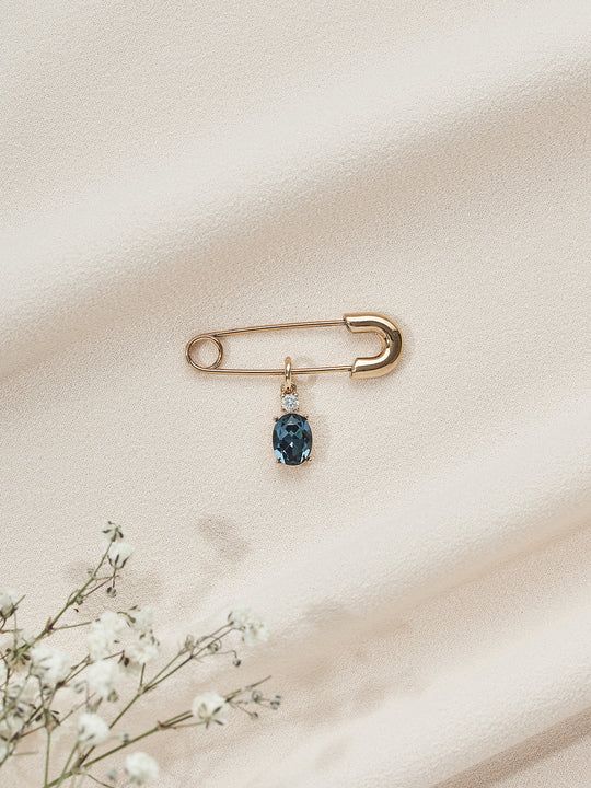 a gold pin with a blue stone sitting on top of white fabric next to flowers