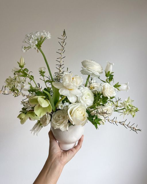 a hand holding a white vase filled with flowers