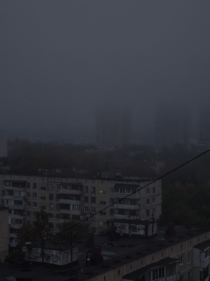 an airplane is flying over the city in the foggy sky, with buildings behind it