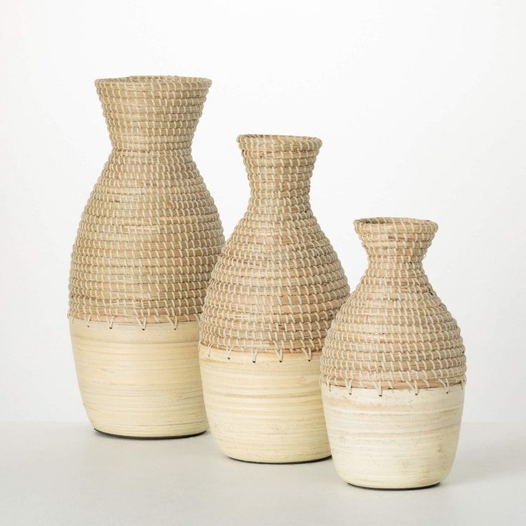 three woven vases are lined up on a white surface, one is made out of straw