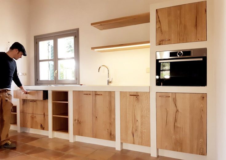 a man standing in a kitchen next to an oven and counter top with wooden cabinets