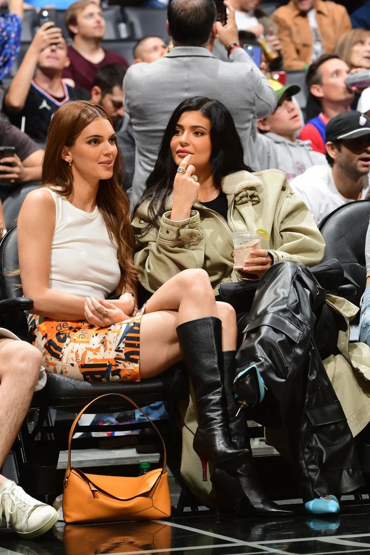 two women sitting next to each other in front of a crowd at a basketball game