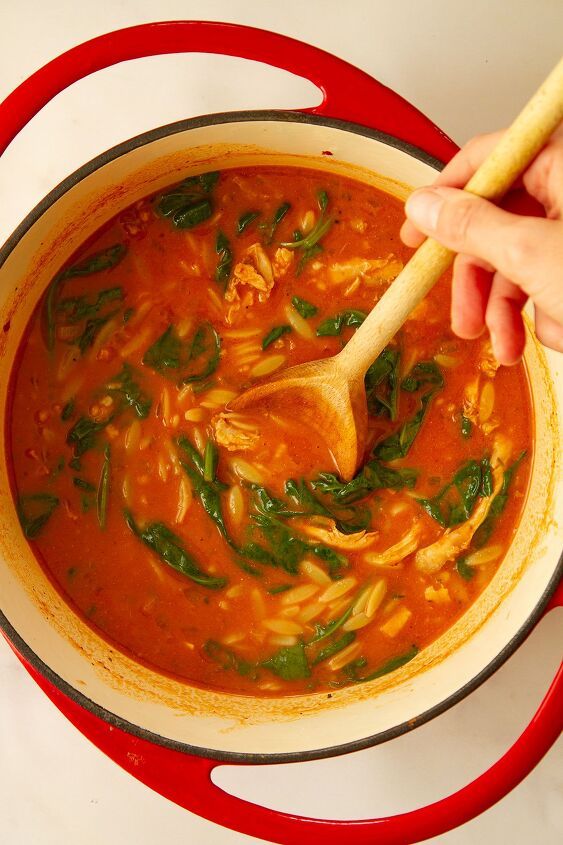 a person stirring a large pot of soup with a wooden spoon in it and spinach on the side