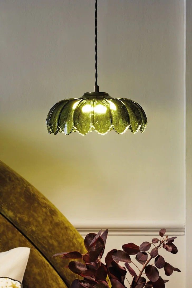 a green lamp hanging over a couch next to a potted plant