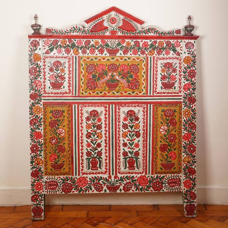 an ornate red and white bed frame with flowers on it's sides, against a white wall