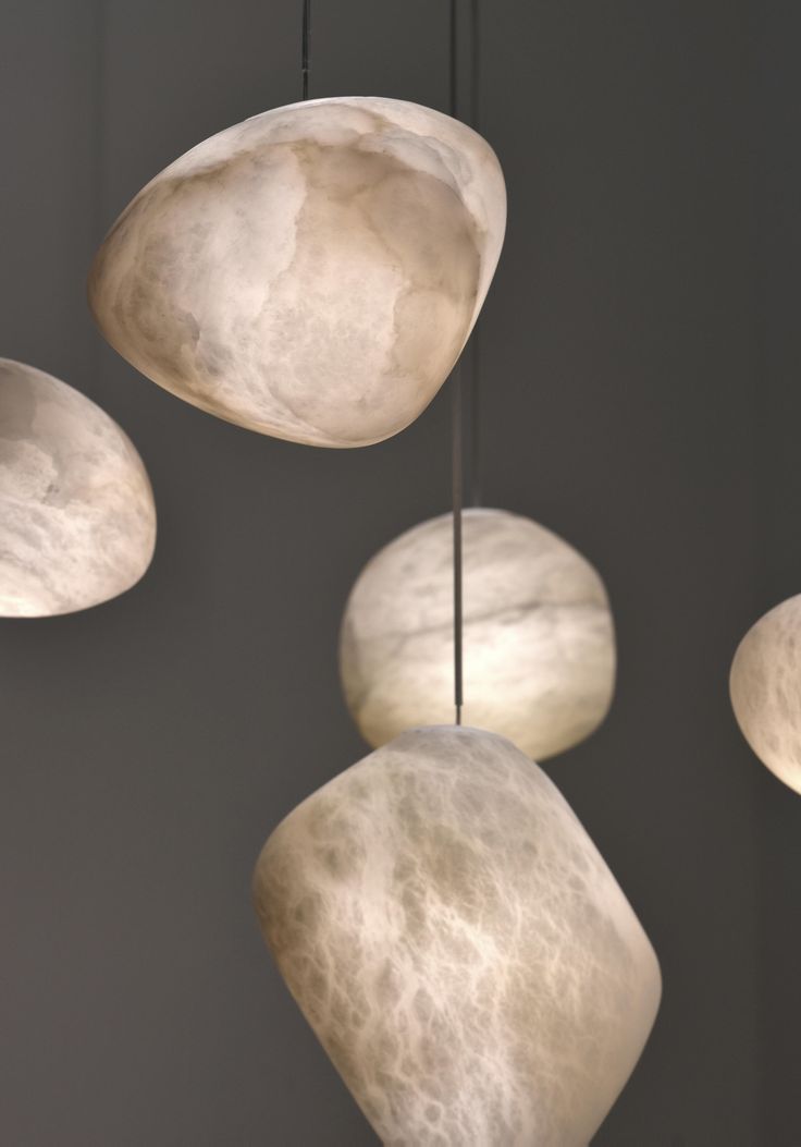 three white lamps hanging from the ceiling in front of a gray wall with four different shades of light on them