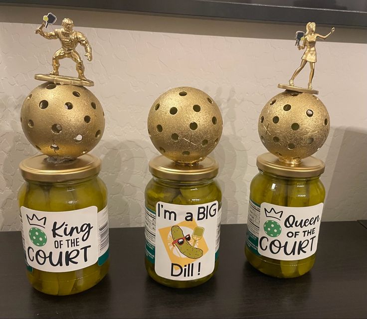 three glass jars with gold lids and small figurines sitting on top of them