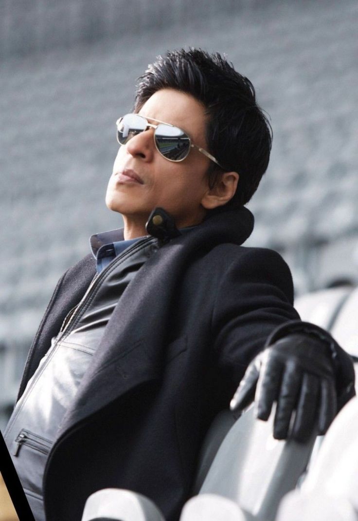 a man wearing sunglasses sitting on top of a white bench in front of an empty bleachers