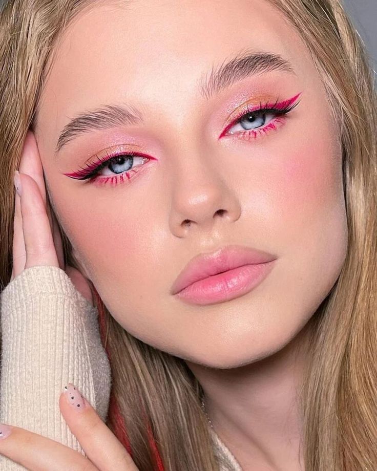 a woman with pink eye makeup holding her hand up to her face and looking at the camera