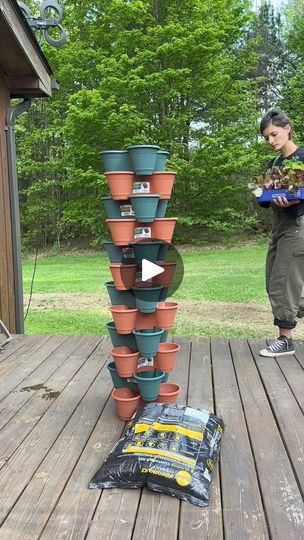 a woman standing next to a stack of potted plants on top of a wooden deck