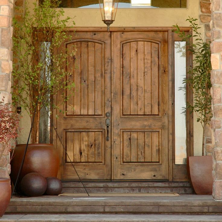 two large wooden doors sitting next to each other on a stone porch with potted plants