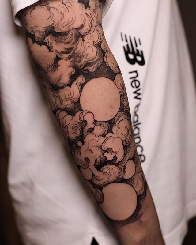 a man's arm with clouds and sun in the sky on his left sleeve